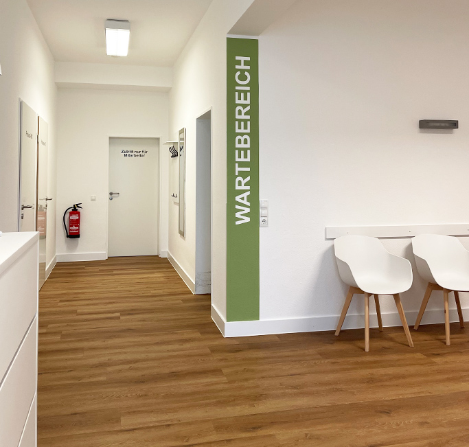 Blick in die hell und modern gestaltete Praxis mit einem Wartebereich für Patienten, der durch einen grünen Streifen an der und dem Schriftzug 