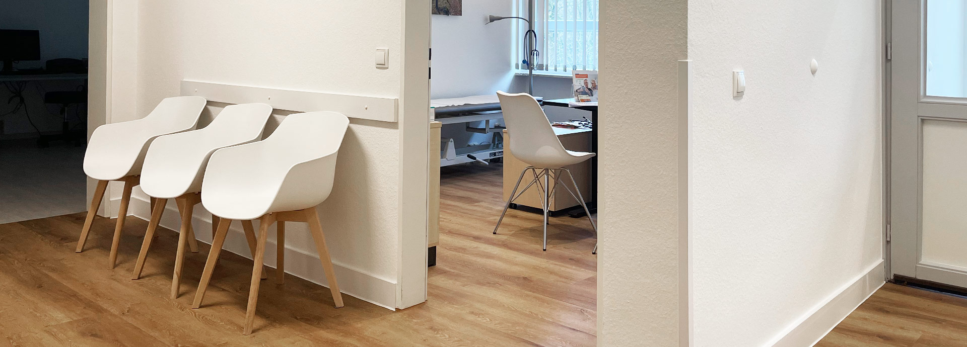 Blick vom Wartebereich der Praxis mit weißen Stühlen in einen modern gestalteten Behandlungsraum der Praxis.